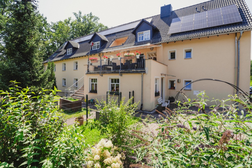 Wohnhaus mit Balkonen, umgeben von hohen Bäumen am Waldrand
