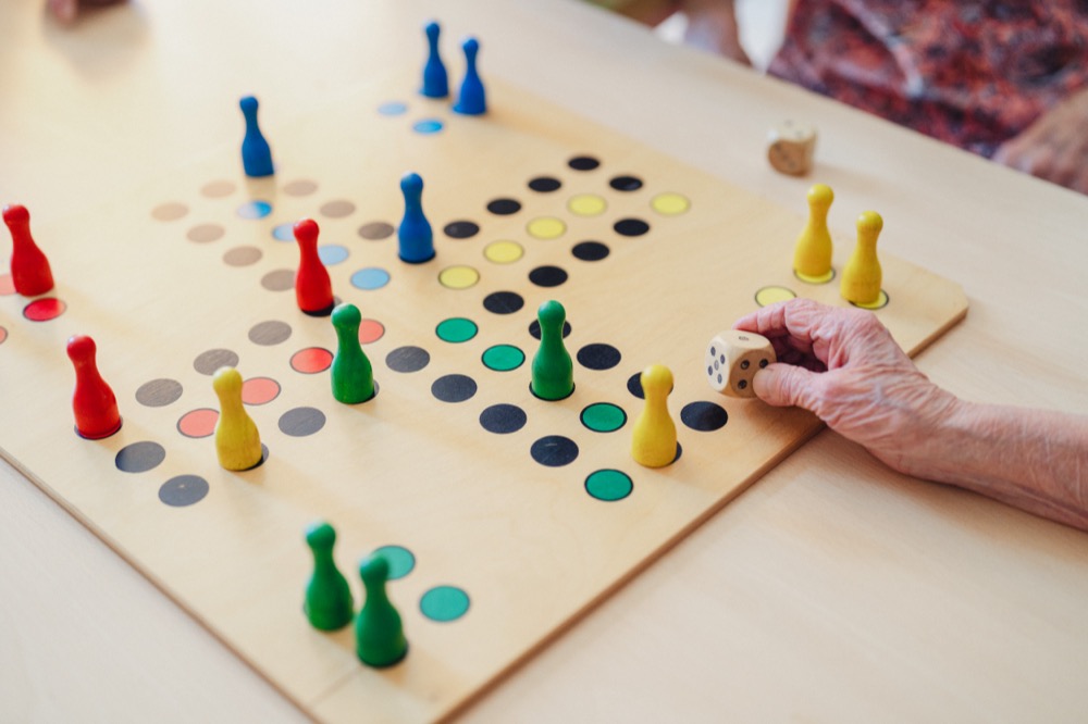 Eine Hand greift den Würfel auf einem angefangenen Brettspiel mit bunten Spielfiguren auf dem Tisch