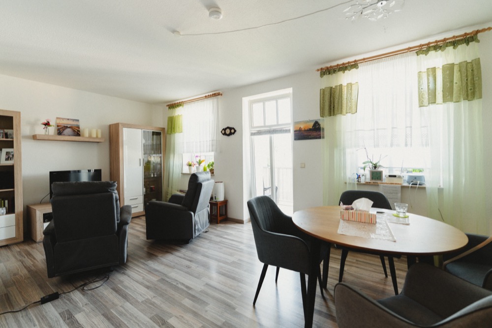 Heller Wohnraum einer Wohnung mit eigenem Esstisch, Sesseln und Balkontür