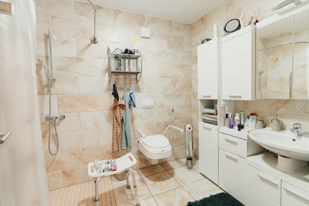 Barrierefreies Bad mit bodengleicher Dusche, Duschhocker, Haltegriffen am WC und Waschtisch