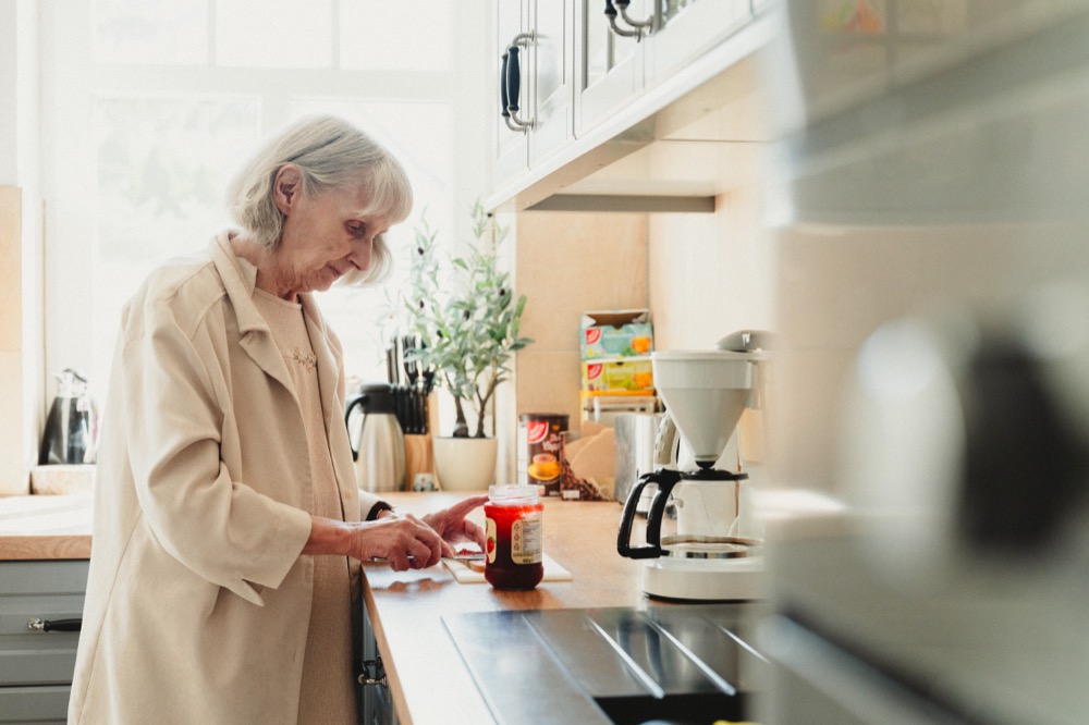 Ältere Dame bereitet sich in ihrer eigenen Küche am Fenster eine Mahlzeit zu