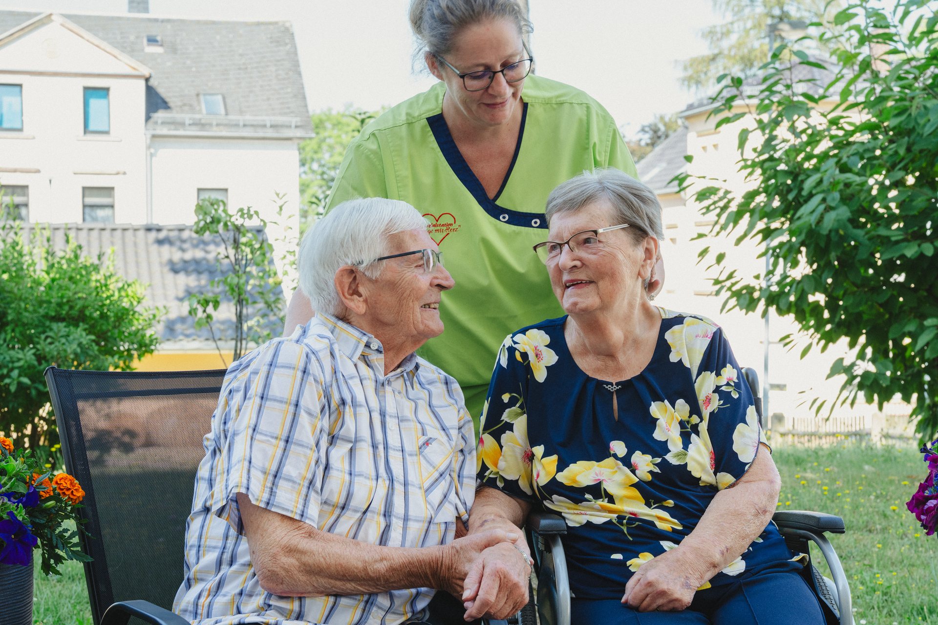 Ehepaar im Garten, begleitet von einer Pflegekraft